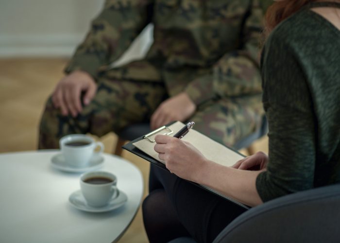 Close-up of psychologist writing down notes while talking to her patient from army